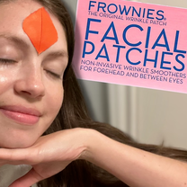 Lesley is smiling with mouth and eyes closed to show off her skin. She is wearing a Frownies wrinkle patch on her forehead. A cutout picture of the Frownies box is edited into the background.